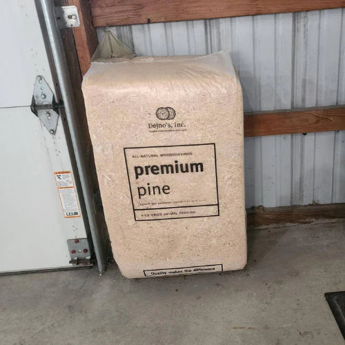 Bag of premium pine wood shavings leaning against a wooden and metal wall. The packaging reads 