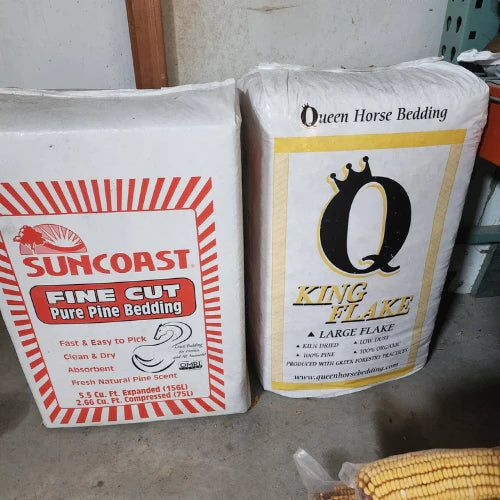 Two bags of horse bedding stand side by side. The left bag is Suncoast Fine Cut Pure Pine Bedding, and the right is Queen Horse Bedding King Flake Large Flake.